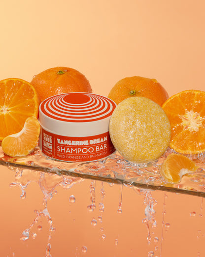 A shampoo bar named Tangerine Dream placed beside sliced oranges, with water droplets around, indicating a fresh and moisturizing product.